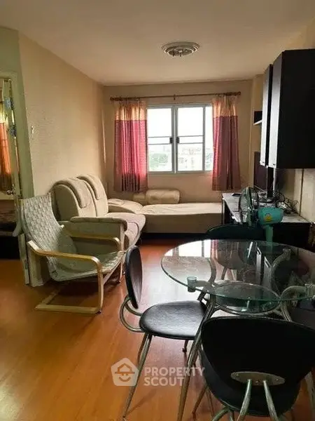 Cozy living room with glass dining table and comfortable seating, featuring large window with natural light.