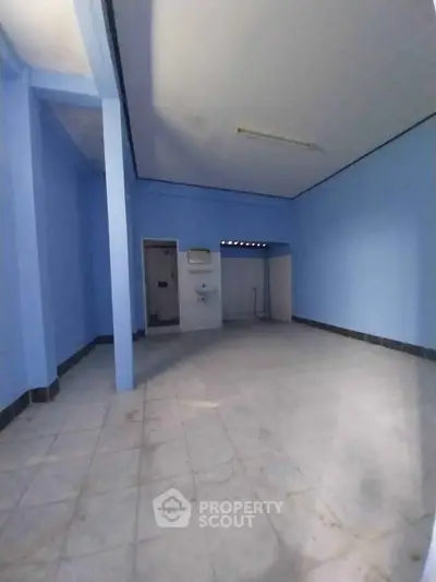 Spacious blue-painted room with tiled floor and high ceiling, ideal for versatile use.