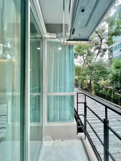 Modern balcony with glass railing and lush greenery view in urban setting.
