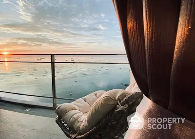 Stunning balcony view with ocean sunset and cozy seating, perfect for relaxation.