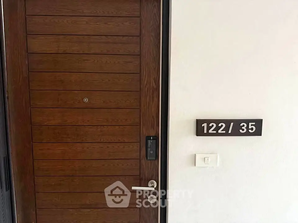 Modern wooden apartment door with digital lock and unit number 122/35 displayed on the wall.