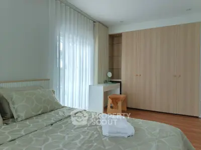 Modern bedroom with stylish decor, featuring a large wardrobe and natural light from a window with sheer curtains.