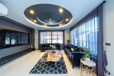 Luxurious modern living room with elegant decor and stylish furniture, featuring a unique ceiling design and large windows.