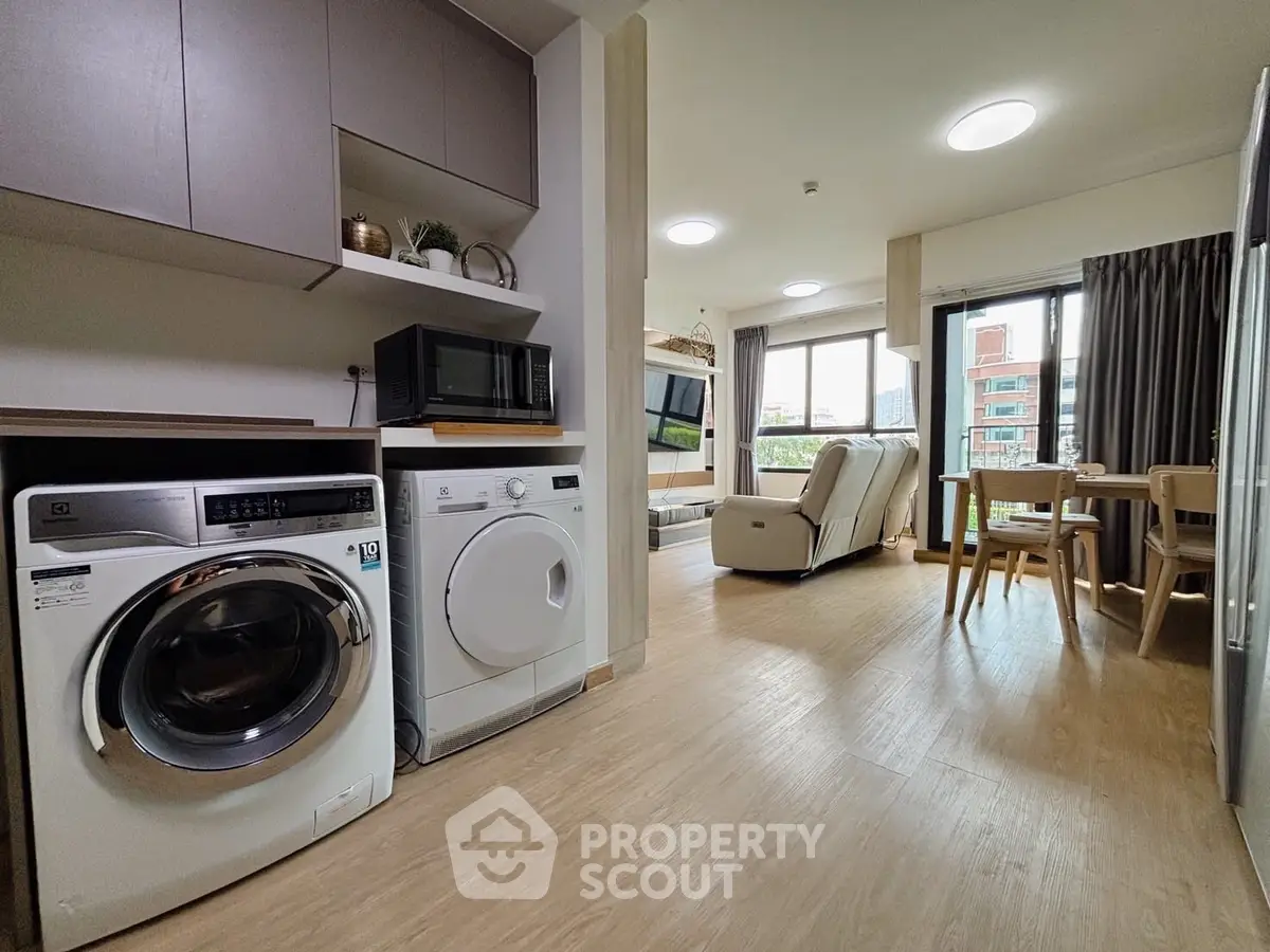 Modern open-plan living area with washing machine and microwave, featuring large windows and stylish decor.