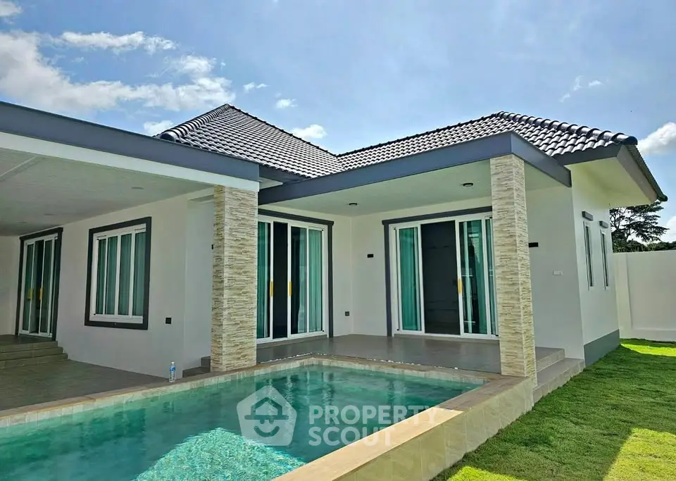 Modern single-story house with private pool and lush green lawn under a clear blue sky.