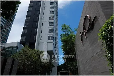 Modern high-rise building with sleek architecture and lush greenery in urban setting.
