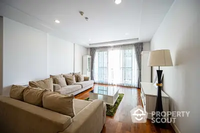 Spacious living room with plush sofas, hardwood floors, and ample natural light streaming through large glass doors leading to a balcony.