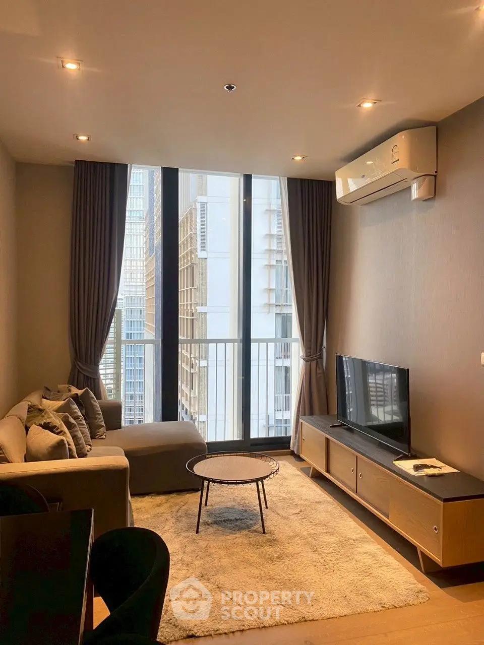 Modern living room with city view, cozy sofa, and sleek TV setup in high-rise apartment.