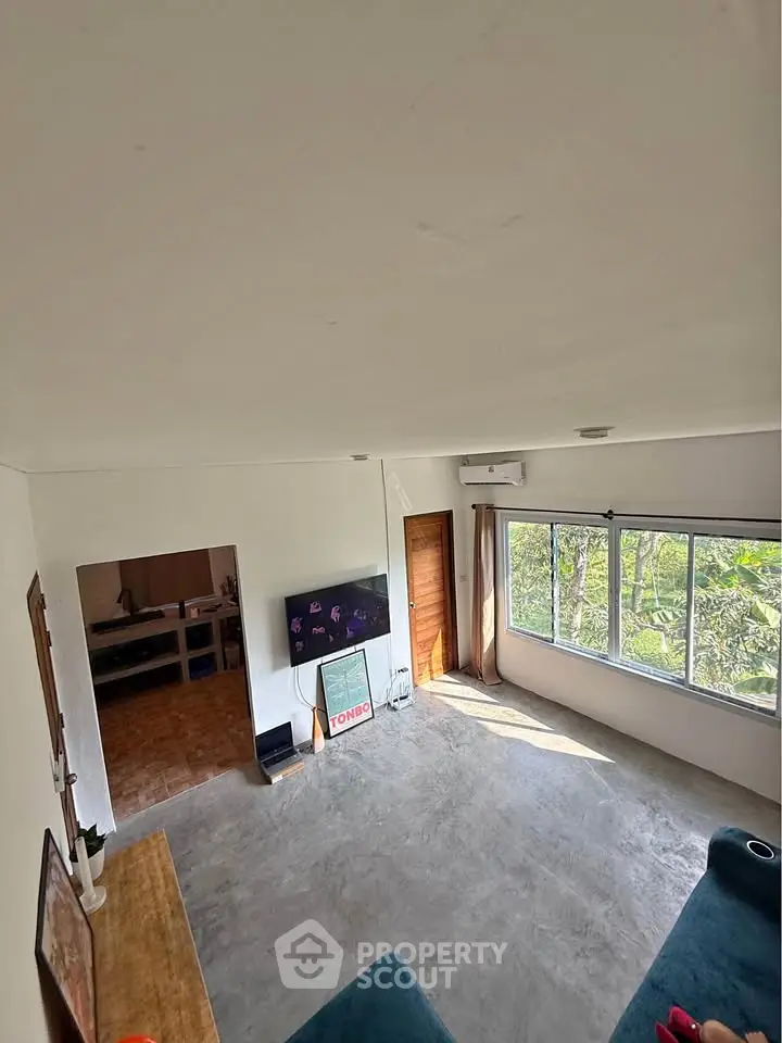 Spacious living room with large windows and natural light, featuring modern decor and greenery view.