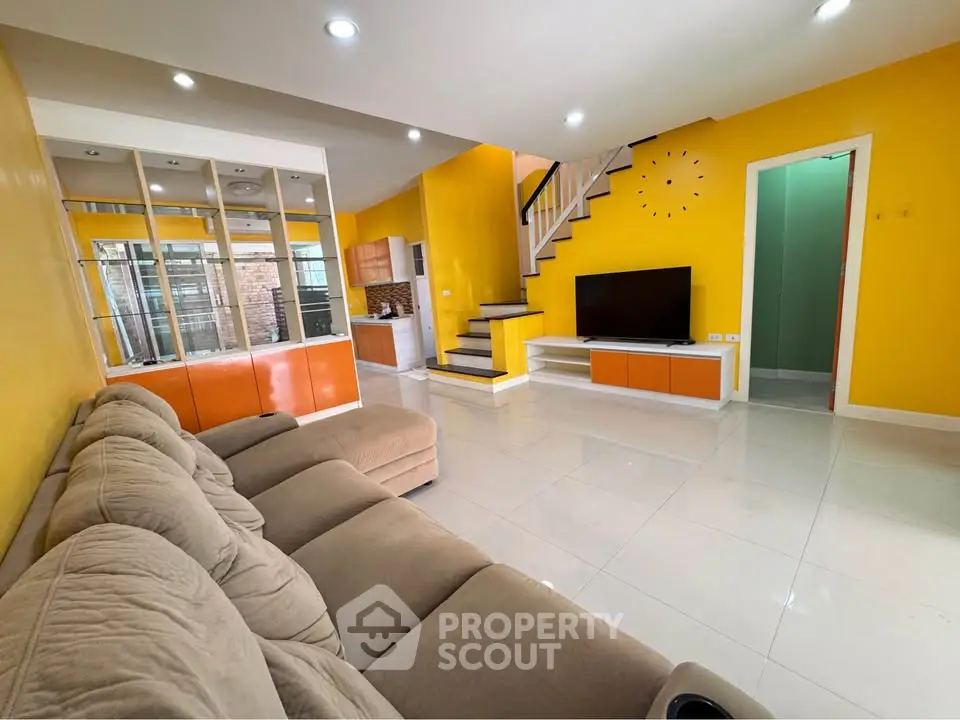 Spacious living room with vibrant yellow walls, modern staircase, and cozy seating area.