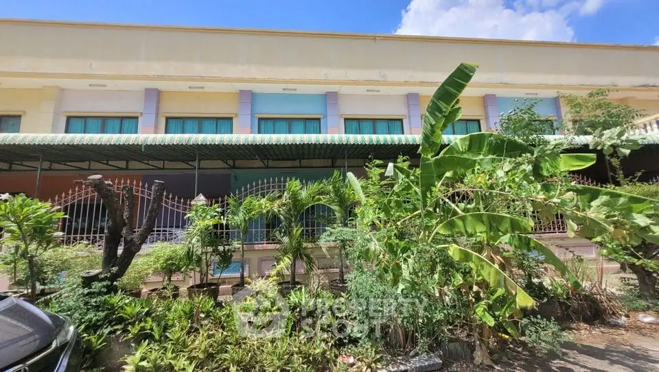 Charming building exterior with lush garden and tropical plants under a clear blue sky.