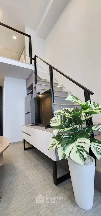 Modern loft interior with stylish staircase and potted plant, featuring sleek design and natural light.
