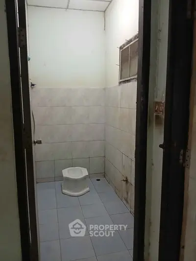 Compact bathroom with squat toilet and tiled walls, ideal for minimalist design enthusiasts.