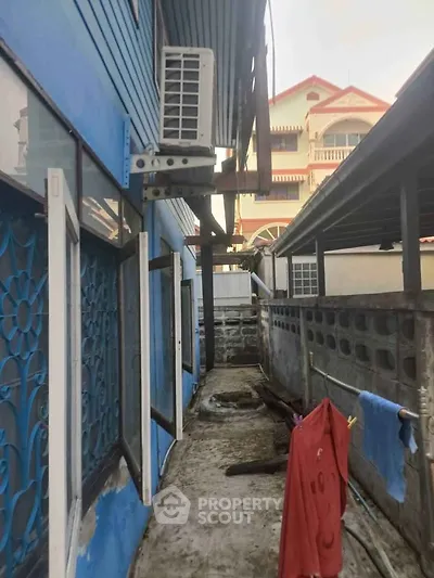 Narrow alleyway between residential buildings with air conditioning unit and blue decorative window grills.