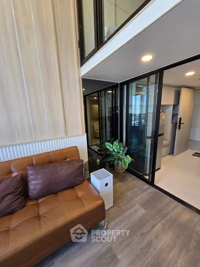 Modern living room with stylish brown sofa and glass doors leading to a sleek kitchen area.