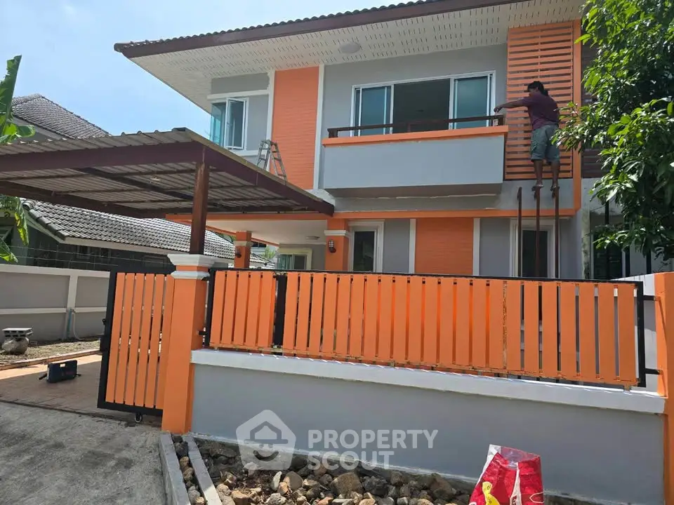 Modern two-story house with orange accents and a carport, showcasing contemporary design and curb appeal.