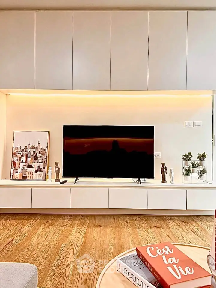 Modern living room with sleek cabinetry and stylish decor, featuring a flat-screen TV and wooden flooring.