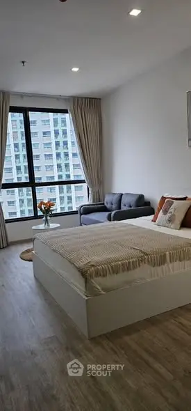 Modern bedroom with city view, cozy seating area, and stylish decor.