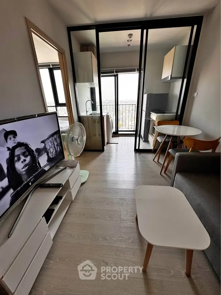 Modern living room with open kitchen and balcony view, featuring sleek furniture and natural light.