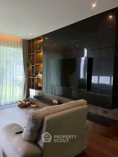 Luxurious living room with modern decor and large TV, featuring floor-to-ceiling windows and elegant shelving.