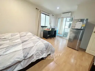 Cozy bedroom with modern decor and workspace, featuring a large window and fridge.