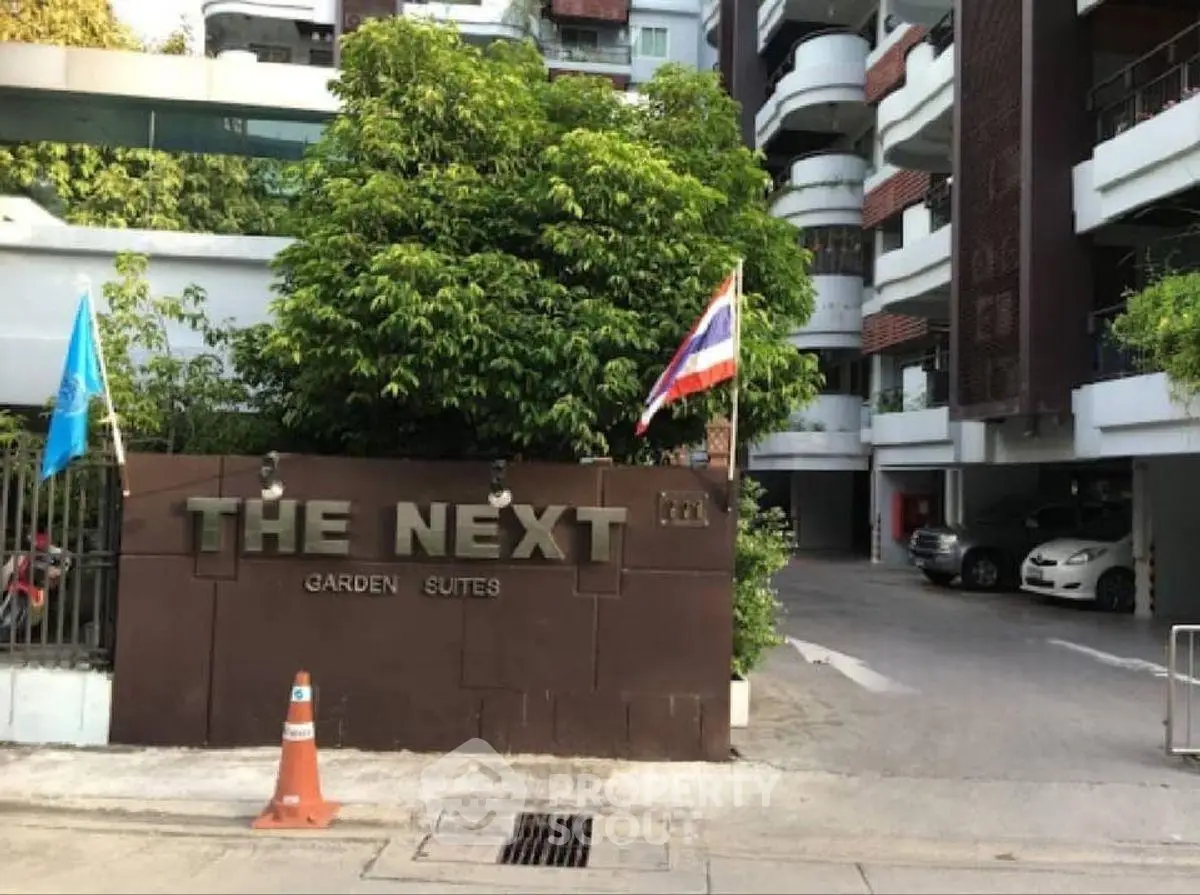 Modern apartment entrance with lush greenery and flags, The Next Garden Suites.