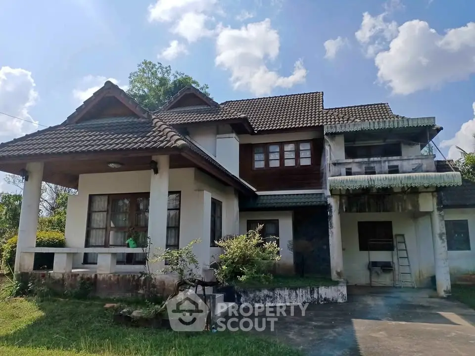 Charming rustic house with tiled roof and lush greenery under a bright blue sky.