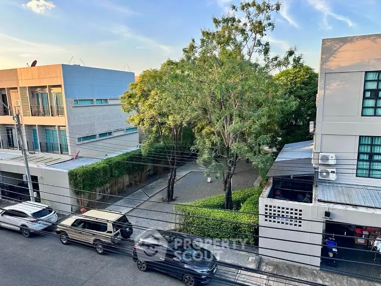 Urban residential area with modern buildings and parked cars, showcasing greenery and clear skies.