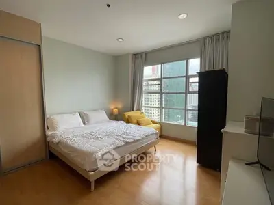 Spacious bedroom with large window offering city views, modern furnishings, and cozy ambiance.