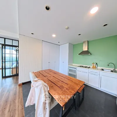 Modern kitchen with wooden table and green accent wall, featuring sleek appliances and open layout.