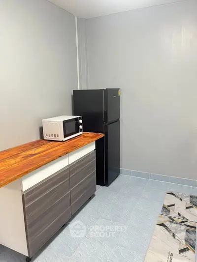 Modern kitchen with sleek cabinets, microwave, and fridge on tiled floor.