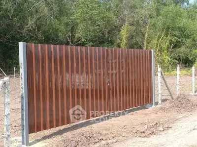 Secure and modern brown metal gate with sturdy concrete posts in a natural setting.