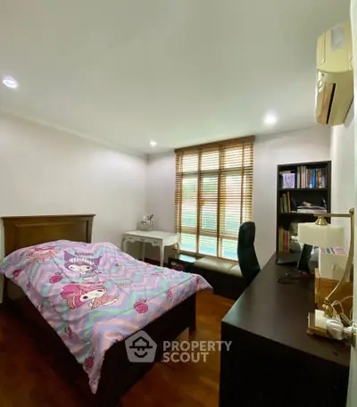 Cozy bedroom with wooden flooring, desk, and large window with blinds.