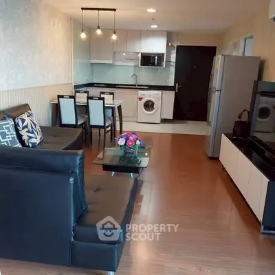 Modern open-layout living room with kitchen, featuring sleek furniture and appliances.
