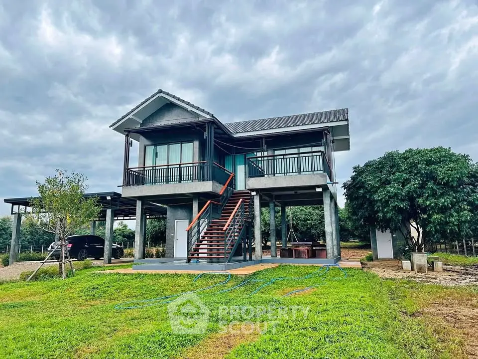 Charming elevated house with lush garden and spacious balcony under cloudy sky.