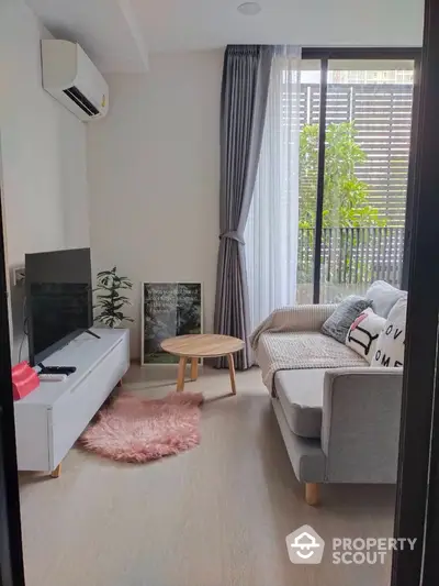 Cozy and modern living room with natural light, plush sofa, and sleek entertainment unit, leading to a serene balcony with greenery.