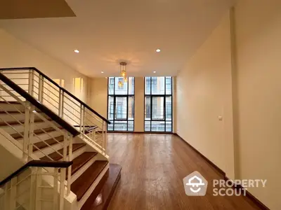 Spacious two-level living area with gleaming hardwood floors, large windows allowing ample natural light, and an elegant staircase leading to an upper level, perfect for modern urban living.