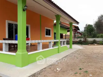 Charming single-story home with vibrant orange and green exterior, spacious porch, and lush surroundings.