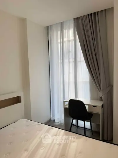 Cozy bedroom with study nook and natural light through large window.