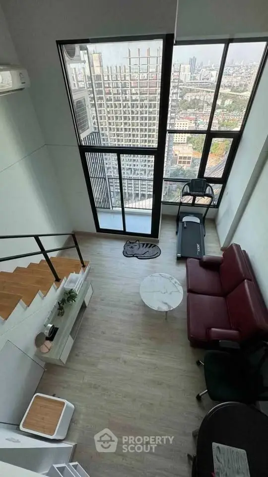 Modern loft apartment with high ceilings and city view, featuring a cozy living area and treadmill.