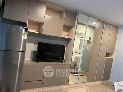 Modern living room with sleek cabinetry and mirrored wardrobe, featuring a stainless steel fridge and TV setup.