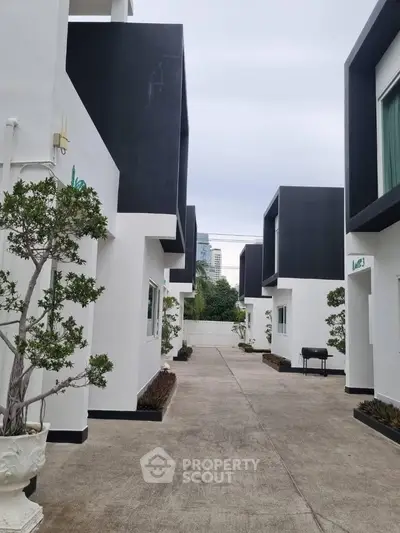 Modern townhouse complex with sleek black and white design, featuring landscaped pathways and urban backdrop.