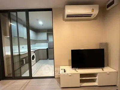 Modern living room with sliding glass doors to a sleek kitchen featuring a washing machine and air conditioning.
