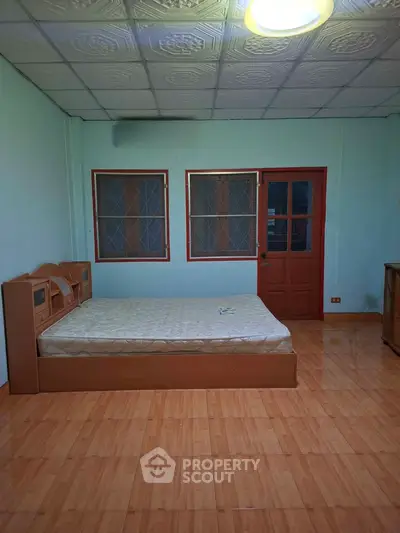 Spacious bedroom with wooden flooring and large windows for natural light.