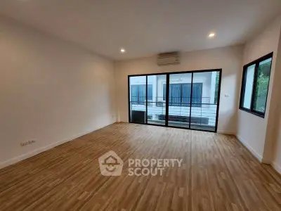 Spacious empty room with wooden flooring and large windows, perfect for customization.