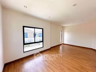 Spacious empty room with wooden flooring and large window, perfect for customization.