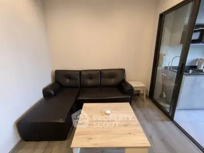 Cozy living room with black leather sofa and wooden coffee table, adjacent to a modern kitchen.