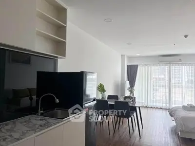 Modern open-plan living room with kitchen and dining area, featuring large windows and stylish decor.
