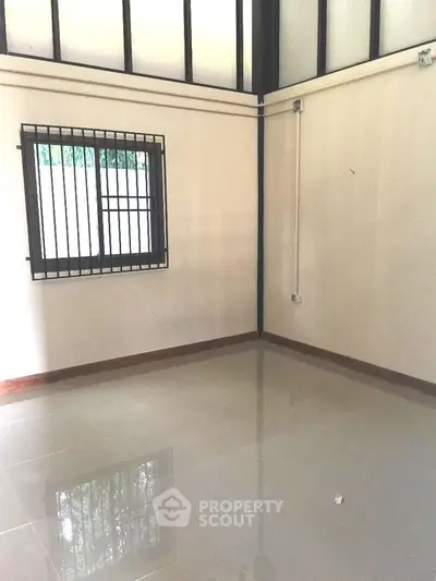 Spacious empty room with glossy tiled floor and barred window