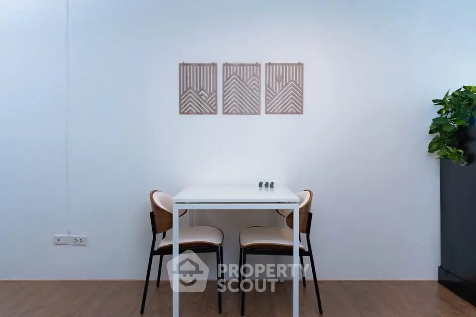 Minimalist dining area with white table and chairs, modern wall art, and wooden flooring.